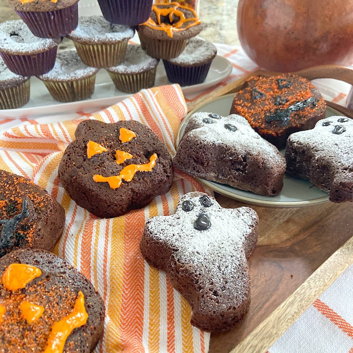 Chocolate brownies decorated with Halloween pumpkin and ghost designs on plates with orange striped napkin