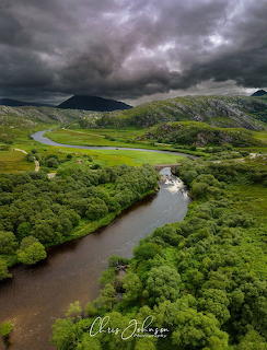 Winding river through a green Scottish valley under dark storm clouds