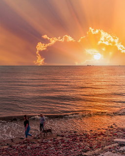 Sunset rays over a calm ocean with two people on a rocky beach