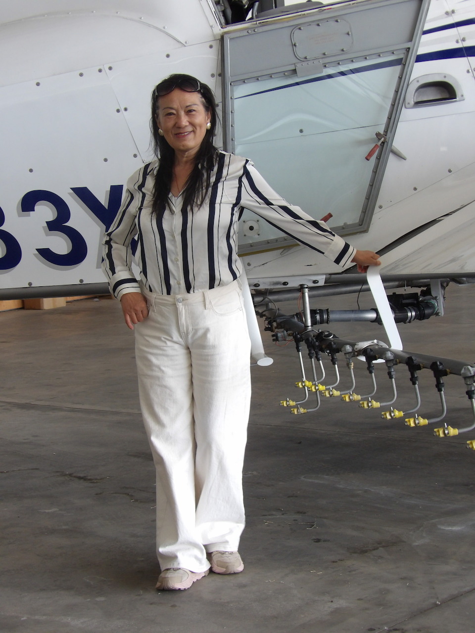 Woman smiling next to a spray plane with nozzles visible on the wing inside a hangar