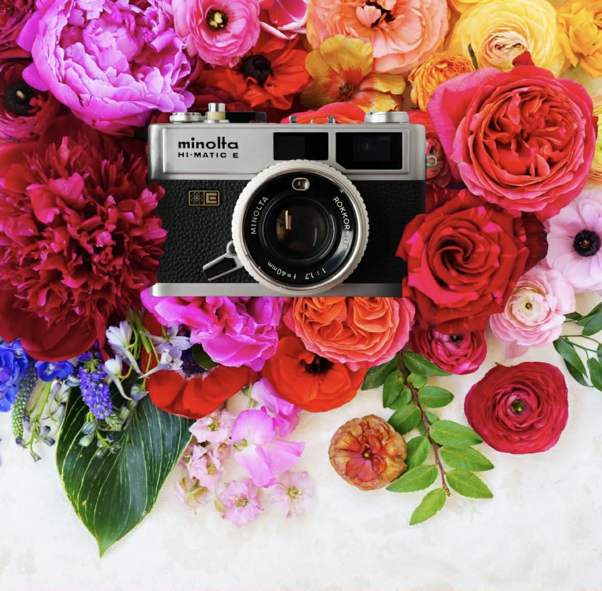 Vintage film camera surrounded by colorful flowers on a white background