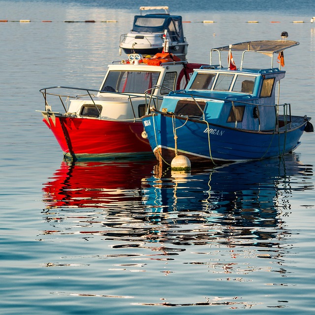 Two colorful fishing boats moored on calm water with their reflections