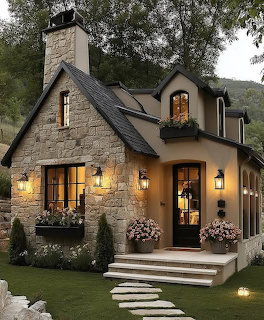 Stone cottage with glowing windows and lanterns surrounded by trees and garden at dusk