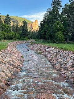 Stone-lined stream flowing through a forested valley with distant sunlit cliffs
