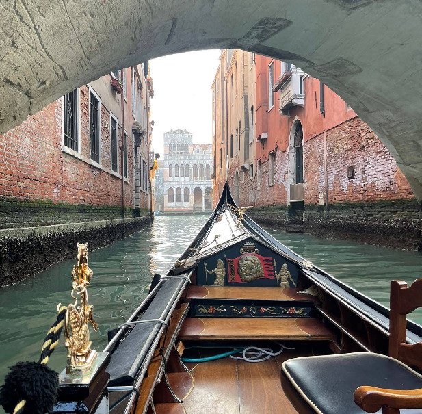 View from a gondola under a bridge on a narrow Venice canal with old brick buildings
