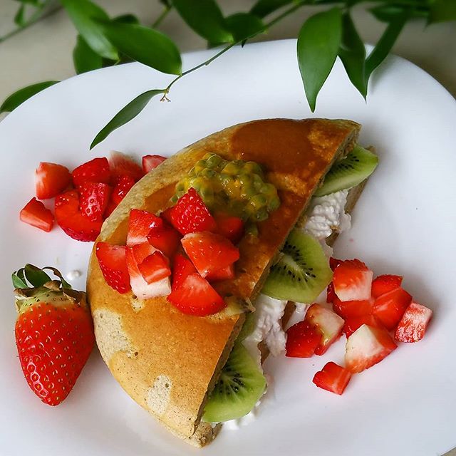 Crepe with strawberries, kiwi, and cream on white plate with green leaf garnish