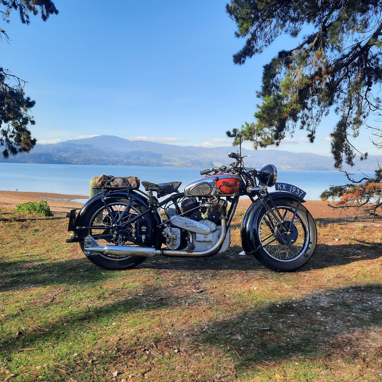 Vintage Royal Enfield motorcycle parked by a lakeshore under pine trees