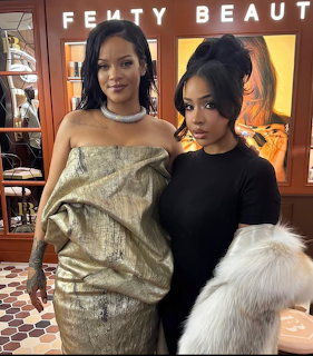 Rihanna in gold dress and diamond choker posing with woman in black outfit at Fenty Beauty event
