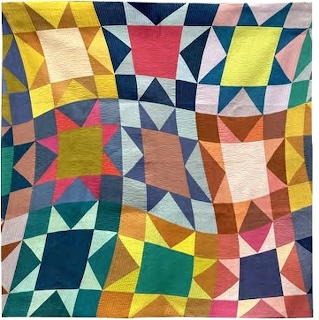 Colorful geometric quilt with triangular and square patchwork blocks in yellow, teal, pink, orange, and navy fabric