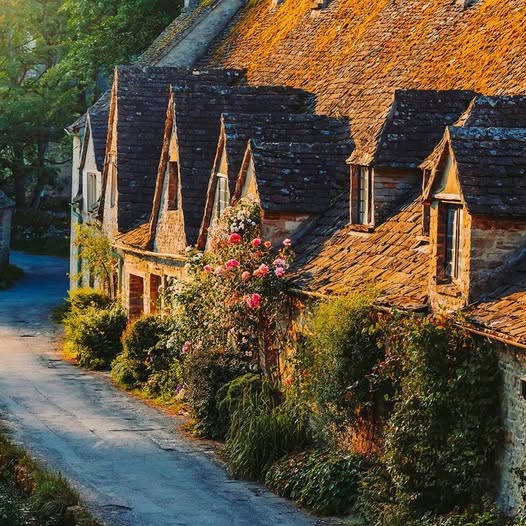 Sunlit old stone cottages with steep roofs along a quiet lane at Arlington Row in Bibury