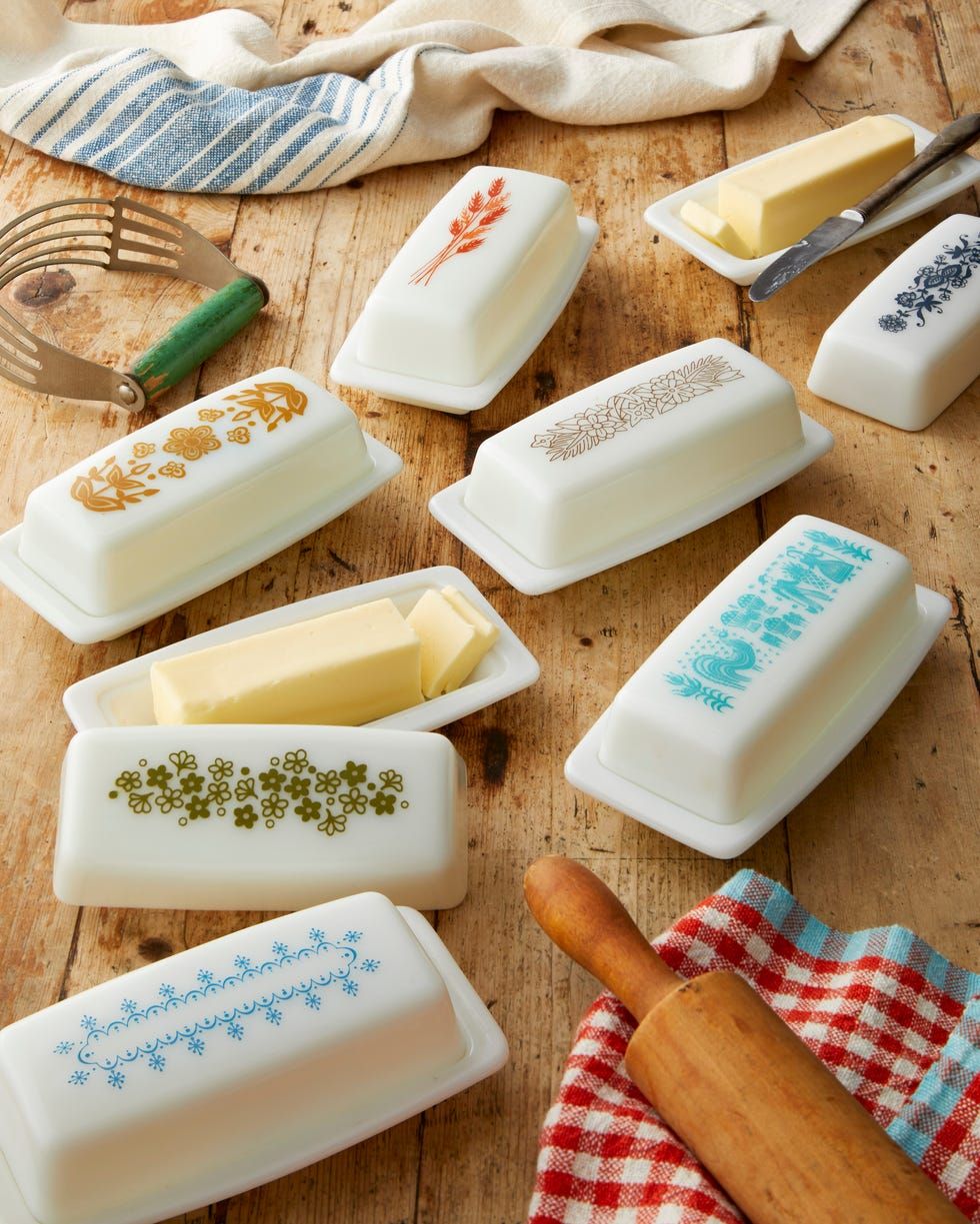 Vintage ceramic butter dishes with floral designs on a rustic wooden table with butter and kitchen linens