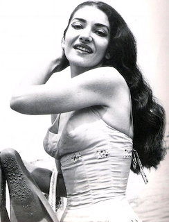 Black and white photo of Maria Callas smiling in a strapless top with long flowing dark hair