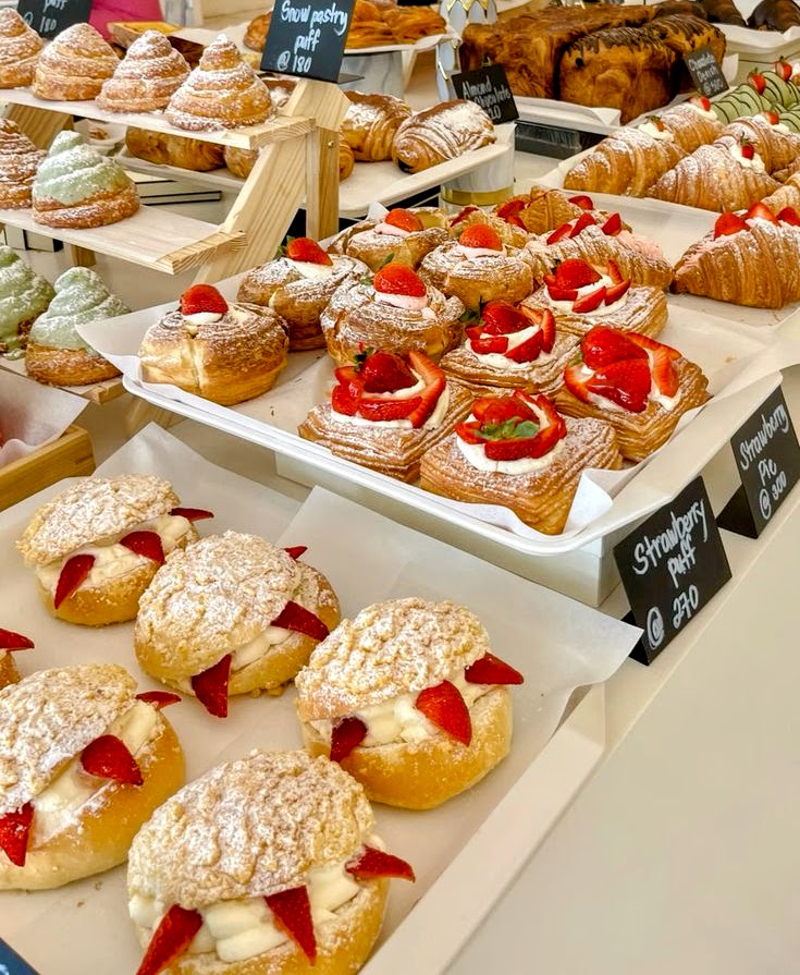 Bakery display with strawberry cream puffs, eclairs, croissants and assorted pastries on white trays