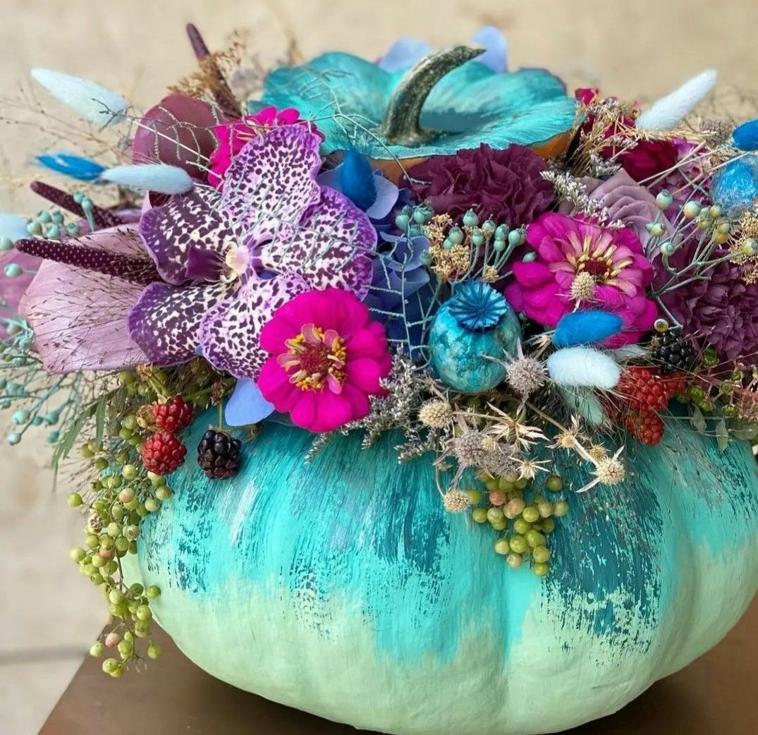 Turquoise pumpkin decorated with colorful feathers, pink flowers, and ornamental accents
