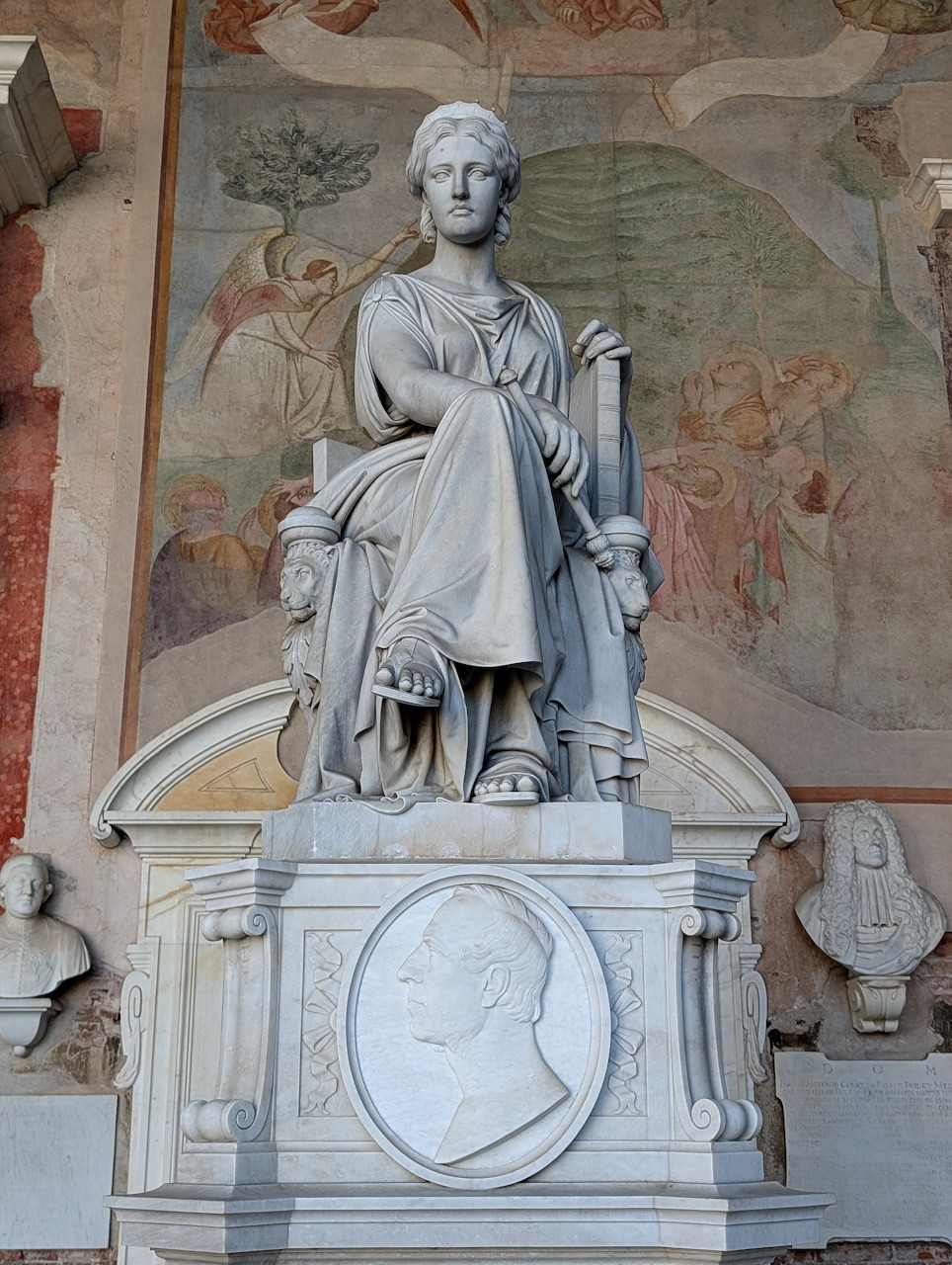 Classical marble statue on decorative pedestal against wall with weathered frescoes