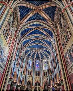Ornate gothic church interior with blue star-painted vaulted ceiling, colorful columns, and tall stained glass windows