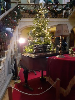 Victorian mansion hall with lit Christmas tree, grand staircase, red carpet, and festive decorations