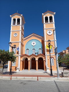 Peach-colored Greek Orthodox chapel with twin bell towers against a clear blue sky