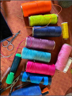 Colorful thread spools, scissors, and fabric pieces on brown leather surface