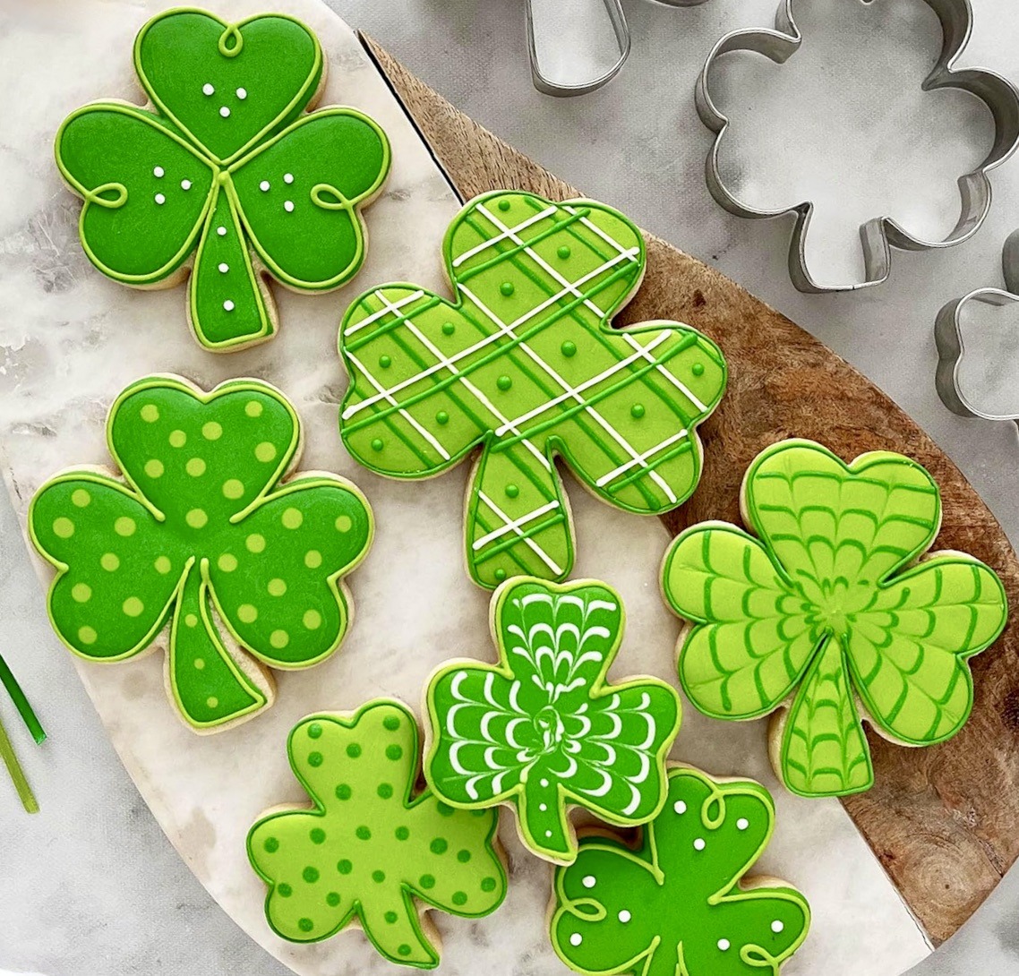 Green shamrock cookies with white icing patterns and metal cookie cutters on a white plate