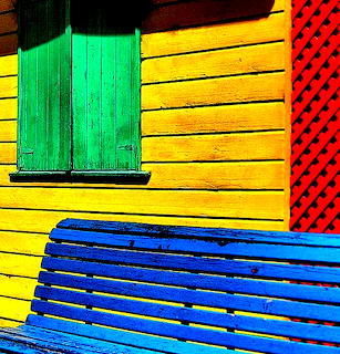 Colorful wooden building with yellow wall, green shutters, blue bench, and red lattice