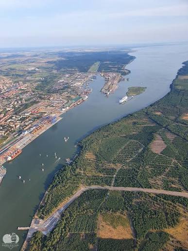 Aerial view of a river with a port area, cargo ship, and forested banks