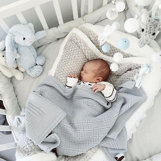 Newborn baby sleeping peacefully in white crib with gray blankets and stuffed animals