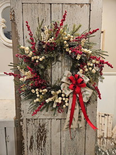Christmas wreath with red berries and pinecones on rustic white wooden door with red bow