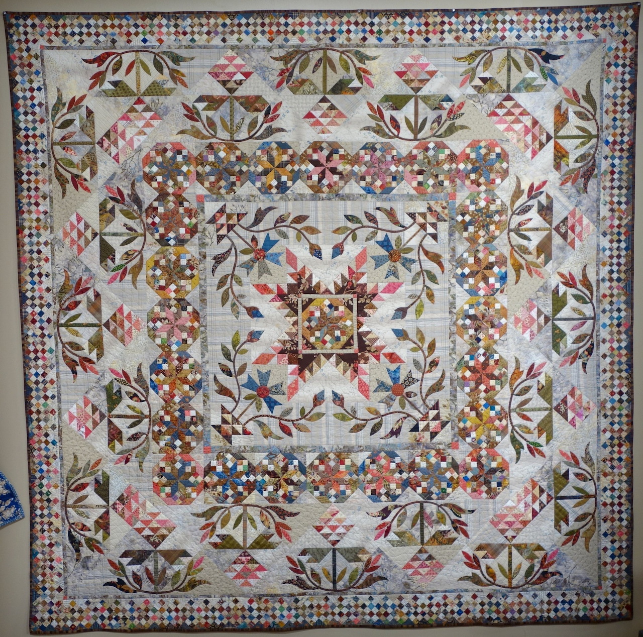 Patchwork quilt with floral medallion design and checkered border hanging on wall