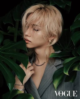 Felix of Stray Kids in a grey blazer with jewelry, surrounded by tropical leaves, on a Vogue cover