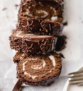 Sliced chocolate Swiss roll cake with chocolate coating and sprinkles beside a fork