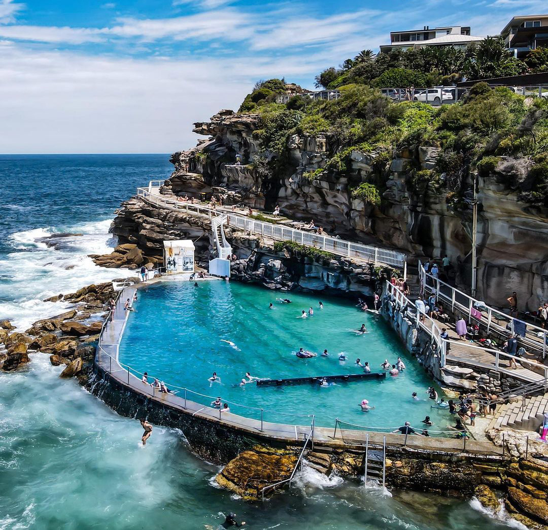 Ocean rock pool beside rocky cliffs with swimmers in turquoise water at Bronte, Sydney