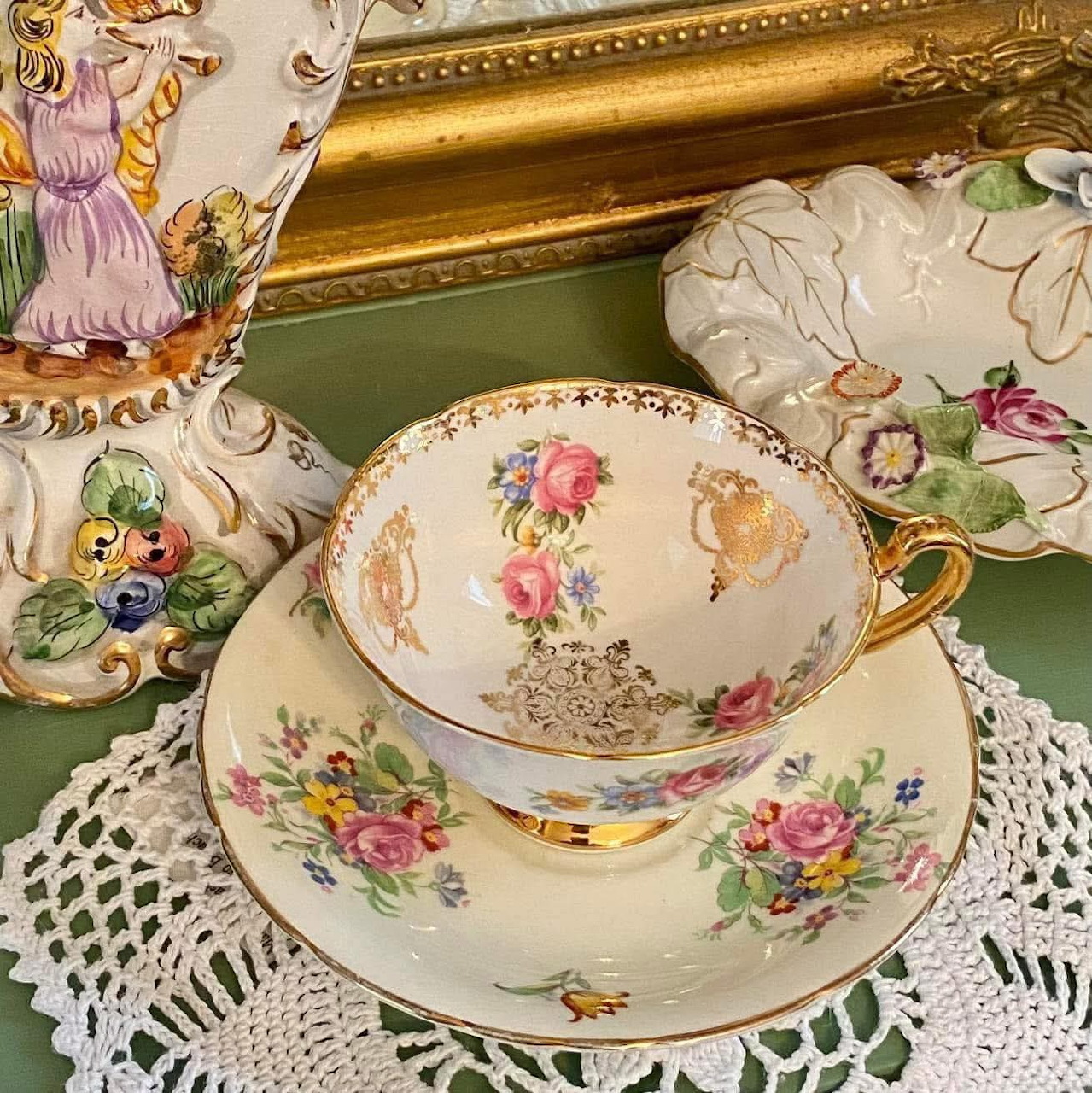 Vintage floral teacup and saucer with gold trim on a lace tablecloth beside matching china