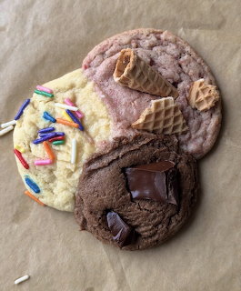 Three large decorated cookies with sprinkles, waffle cone pieces, and chocolate on parchment paper