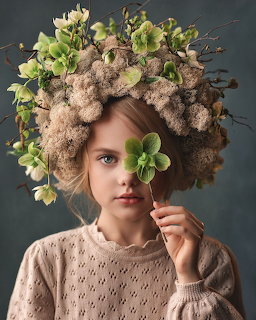 Woman in beige sweater wearing large organic crown of flowers and moss, holding small green flower