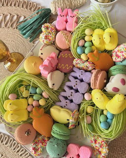 Assortment of pastel Easter candies, marshmallow bunnies and chicks, macarons, and chocolate eggs on wooden board