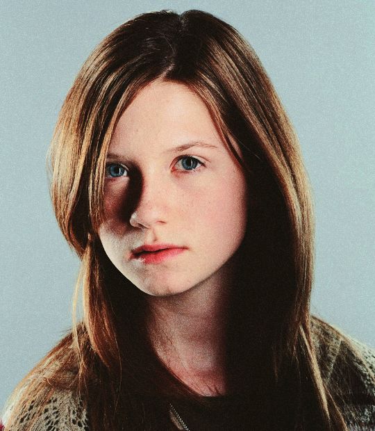 Young woman with long straight auburn hair and blue eyes posing against a teal background