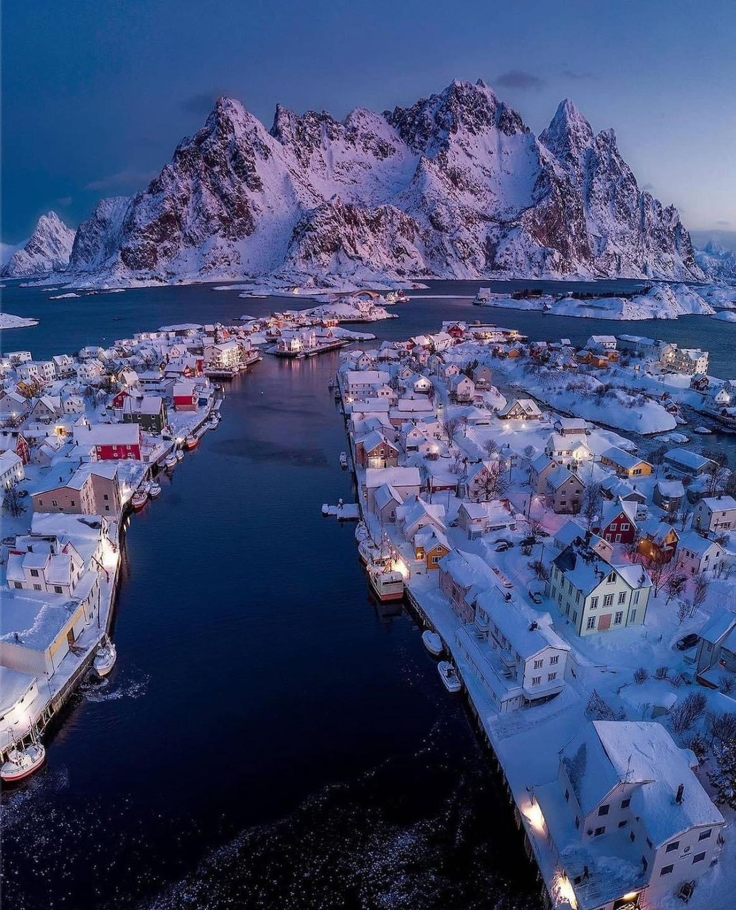 Aerial view of snowy Norwegian fishing village with mountains and fjord at dusk