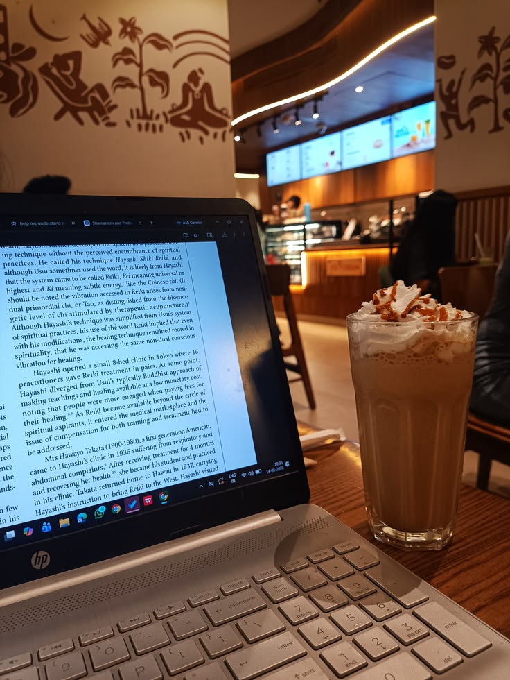 HP laptop with open document next to a tall iced coffee with whipped cream in a café