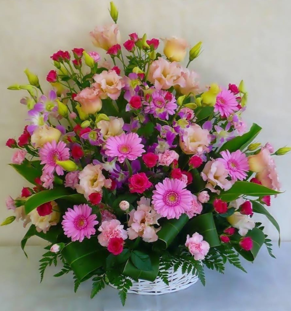 White wicker basket filled with pink gerberas, roses, lisianthus, and purple flowers with green foliage