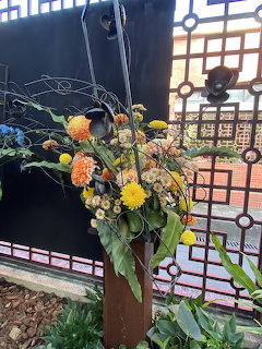 Colorful flower arrangement in a tall vase beside a black metal gate outdoors