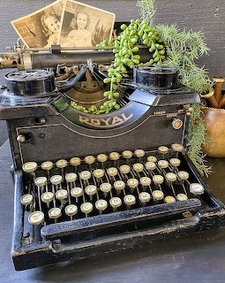 Black vintage Royal typewriter with round keys, succulent plant, and old photos on a table