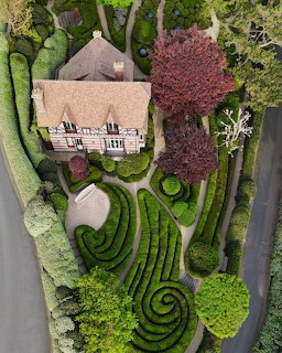 Aerial view of sculpted ornamental gardens with geometric hedges, topiary spheres, and thatched cottage in France