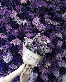 Hand holding a purple flower bouquet in front of a wall of purple and white flowers