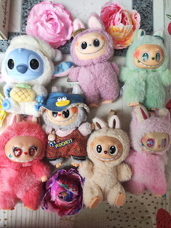 Collection of colorful plush toys and stuffed animals with large eyes arranged on woven surface