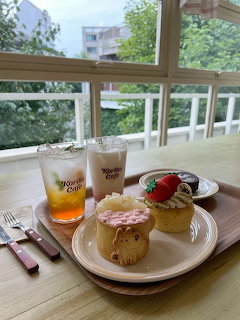 Two decorated cupcakes and iced drinks on a wooden tray at Koriko Cafe, Seoul, with trees visible through windows