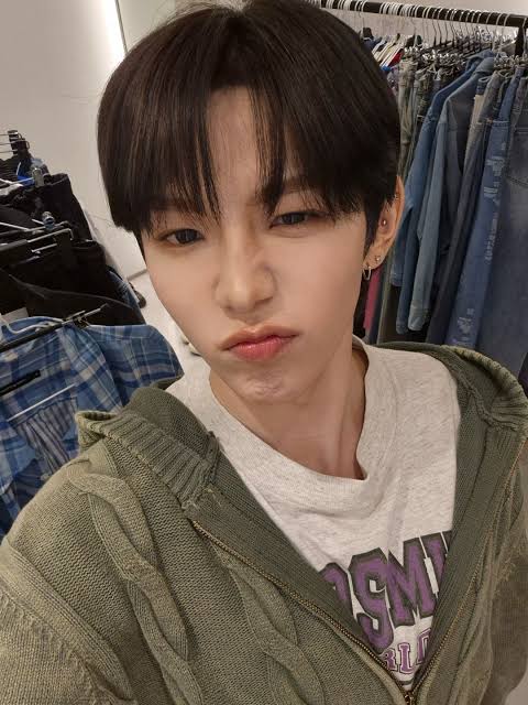 Young man with dark hair making a pout expression, wearing a green hoodie, in a clothing store