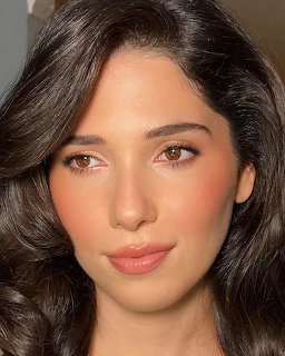 Close-up portrait of a young brunette woman with wavy dark hair and natural makeup