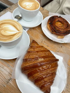 Two latte coffees with a croissant and pastry on a wooden table
