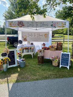 White canopy tent with flower arrangements and potted plants displayed on tables outdoors